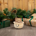 Plush mince pie toy on a wooden floor with Christmas decorations and presents.