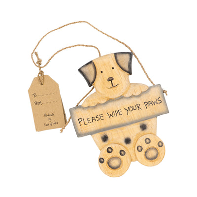 Front facing photo of the wooden sign in the shape of a dog holding a sign that reads 'Please wipe your paws'. The wooden dog has a hanging string attached with a label tied to it, which reads 'To' and 'From' and 'Handmade by East of India'.