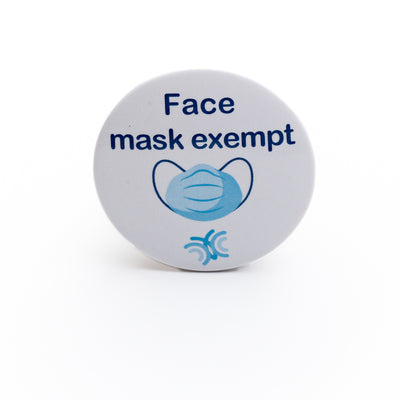 Light blue pin badge featuring dark blue lettered message 'Face mask exempt' and colourful face covering icon on white background