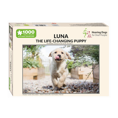 Cream box, on its side, which contains the 1000-piece jigsaw puzzle with a photograph of our a little yellow labrador puppy called Luna happily running with her tongue sticking out.
