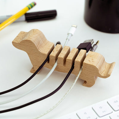 Wooden cable organizer shaped like a dog on a desk with a keyboard and pens in the background.