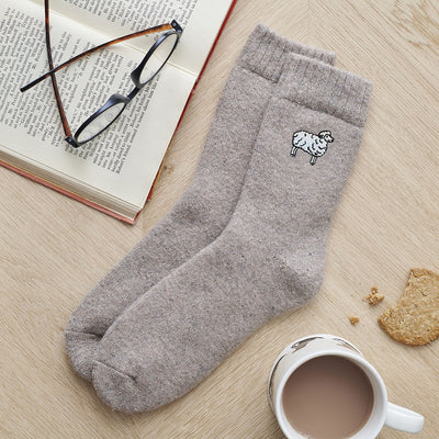 Gray sock with a design on a wooden surface with a book, glasses, and a mug.