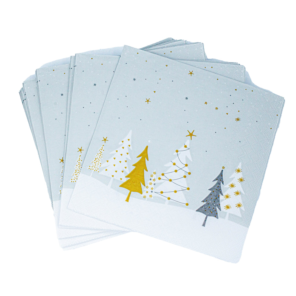 Birds eye view of fanned out grey festive paper napkins, with a contemporary Christmas design. There are white and gold Christmas trees on a snowy surface, underneath a grey sky with stars. 