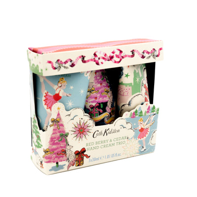 Front on diagonal angle photo of Cath Kidston Christmas Trio of Handcreams in its outer packaging. The box is a cream colour with festive illustrations on the box. E.g. red ribbon, pink Christmas tree, presents and an ice skating figure. The Cath Kidston name is at the bottom of the box with green coloured text that reads: 'Red Berry & Cedar Hand Cream Trio'.