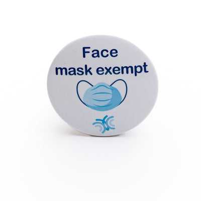 Light blue pin badge featuring dark blue lettered message 'Face mask exempt' and colourful face covering icon on white background