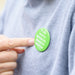 Person pointing to green pin badge on jumper with white lettered message 'If you need to lipread me, please let me know'