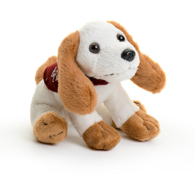 Side shot of a small soft toy dog in a sitting position. The dog looks like it could based on a Spaniel with long ears. The body of the dog is white, the ears, paws and tail are light brown and the dog has brown eyes, a black nose and a mouth sewn in a neutral position. The dog is wearing a miniature burgundy Hearing Dogs jacket.