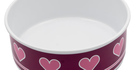 A photograph of a medium sized dog bowl. The inside of the bowl is white and the exterior of the bowl is a dark berry colour with pink hearts with a white outline placed horizontally around the bowl. Underneath the hearts, there is a pink trim with white outline.