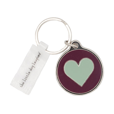 Close up photo of Dog Tag or Keyring. Attached to the metal loop is a maroon coloured circular keyring with a Turquoise Heart design printed on it. Also attached to the metal loop is a silver rectangular dog tag which reads: 'the little dog laughed'. 