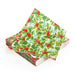 A single napkin with a colourful green and red design of holly and mistletoe leaves and berries on top of a stack of the same napkins.