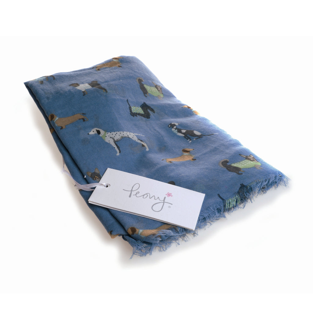 Folded soft looking blue scarf with illustrated dogs of different breeds, such as dalmations, dachshunds and terriers, all over it and Peony label laid on top.