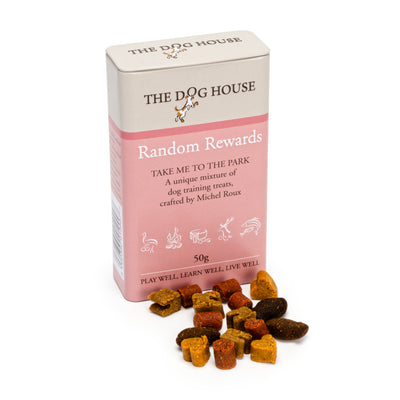 Rectangular pink and cream tin that has the words 'The Dog House Random Rewards' on it with a small pile of treats in front of the tin in five different colours and shapes such as hearts, bones and tubes.